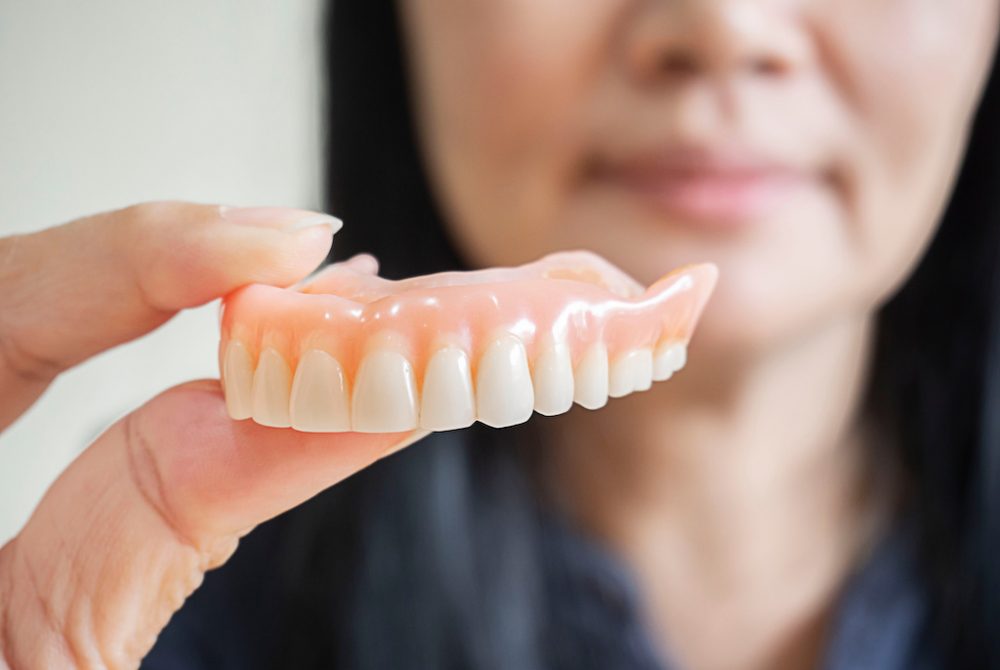 Happy asian woman  be smile and holding dentures in hand. Dentures for prosthetic devices constructed to replace missing teeth and helping to chew food.