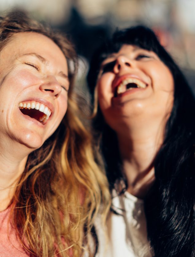 Two cheerful female friends are sharing a moment of joy and laughter, embracing each other outdoors in an urban setting